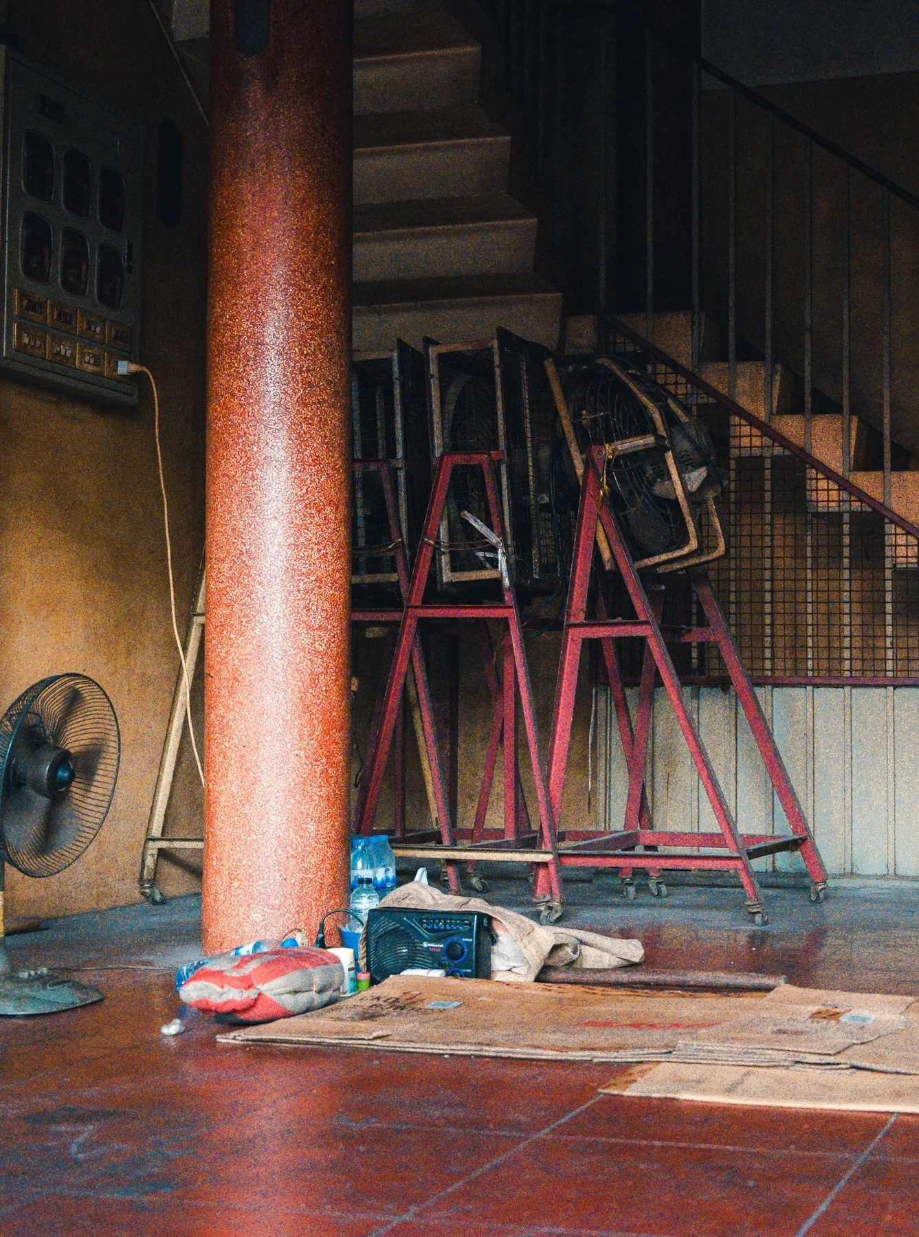 A red column and stacked chairs beneath a dark staircase in Bangkok