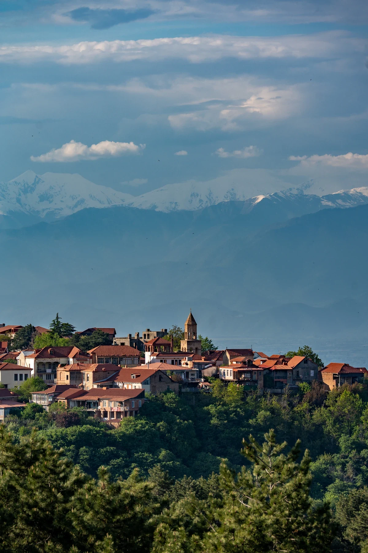 A Georgian town beneath distant mountains and a cloudy blue sky