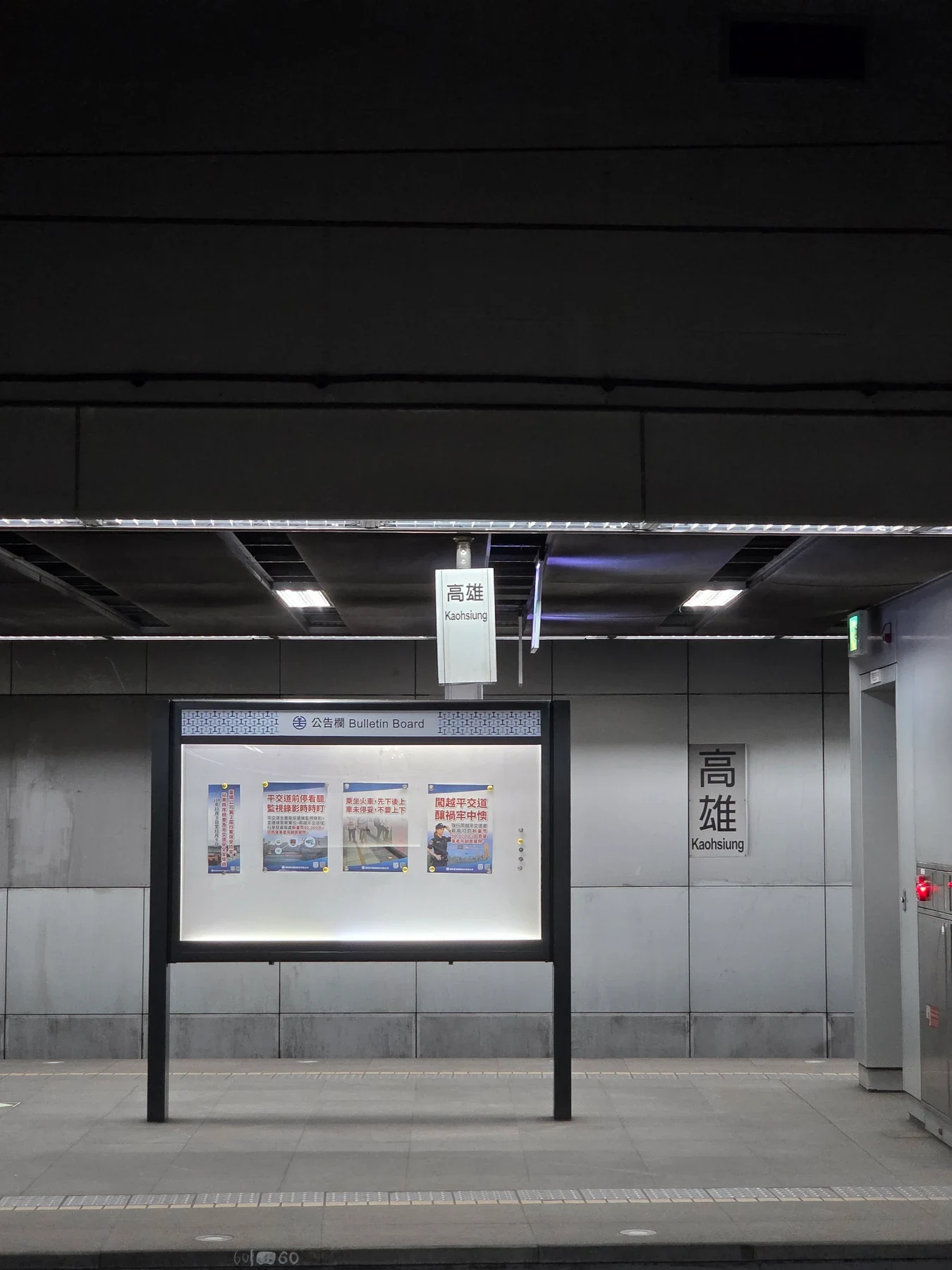 An illuminated bulletin board beneath a large dark ceiling at Kaohsiung station