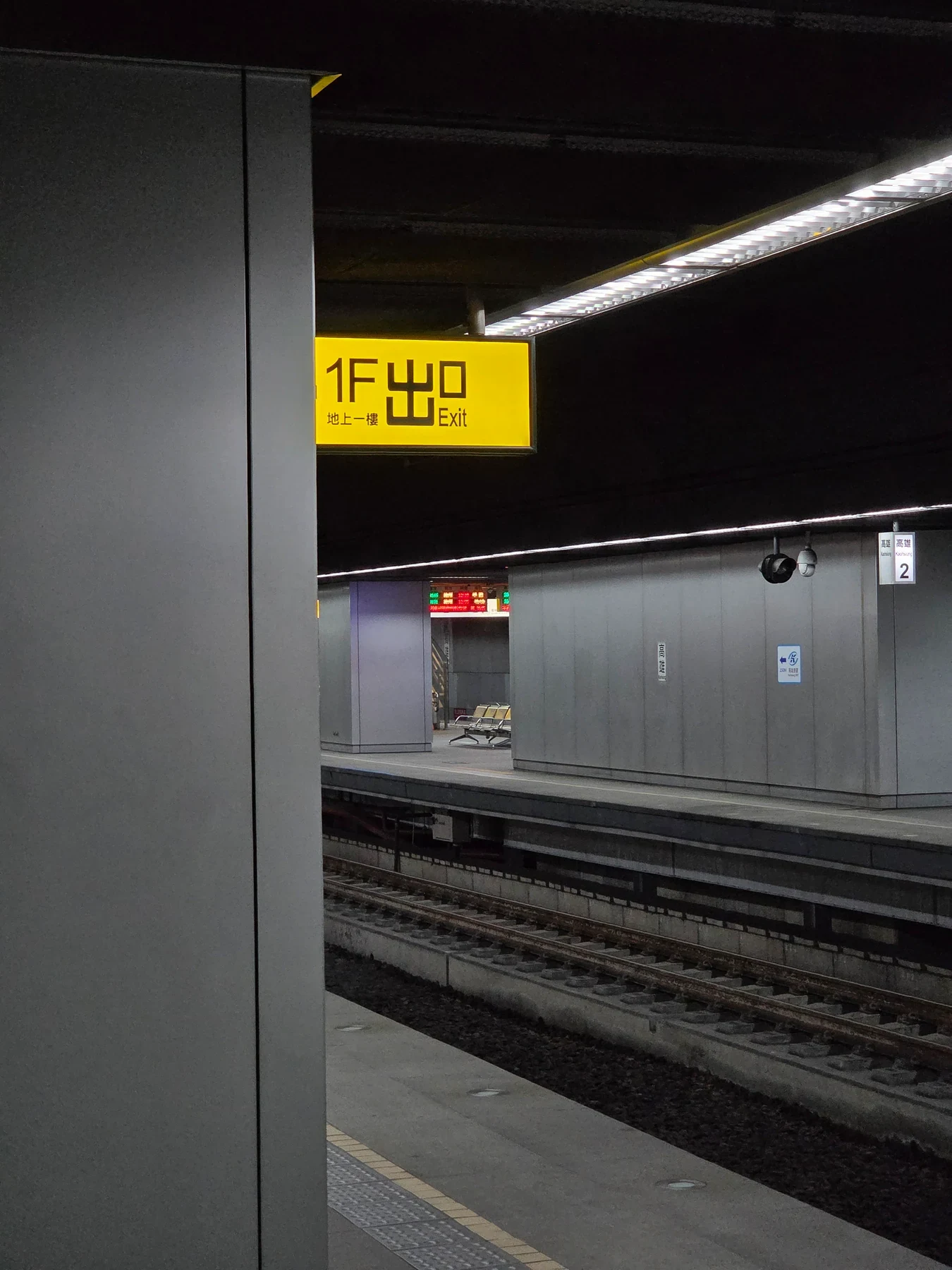 A yellow exit sign beside a pillar and diagonal platform lighting