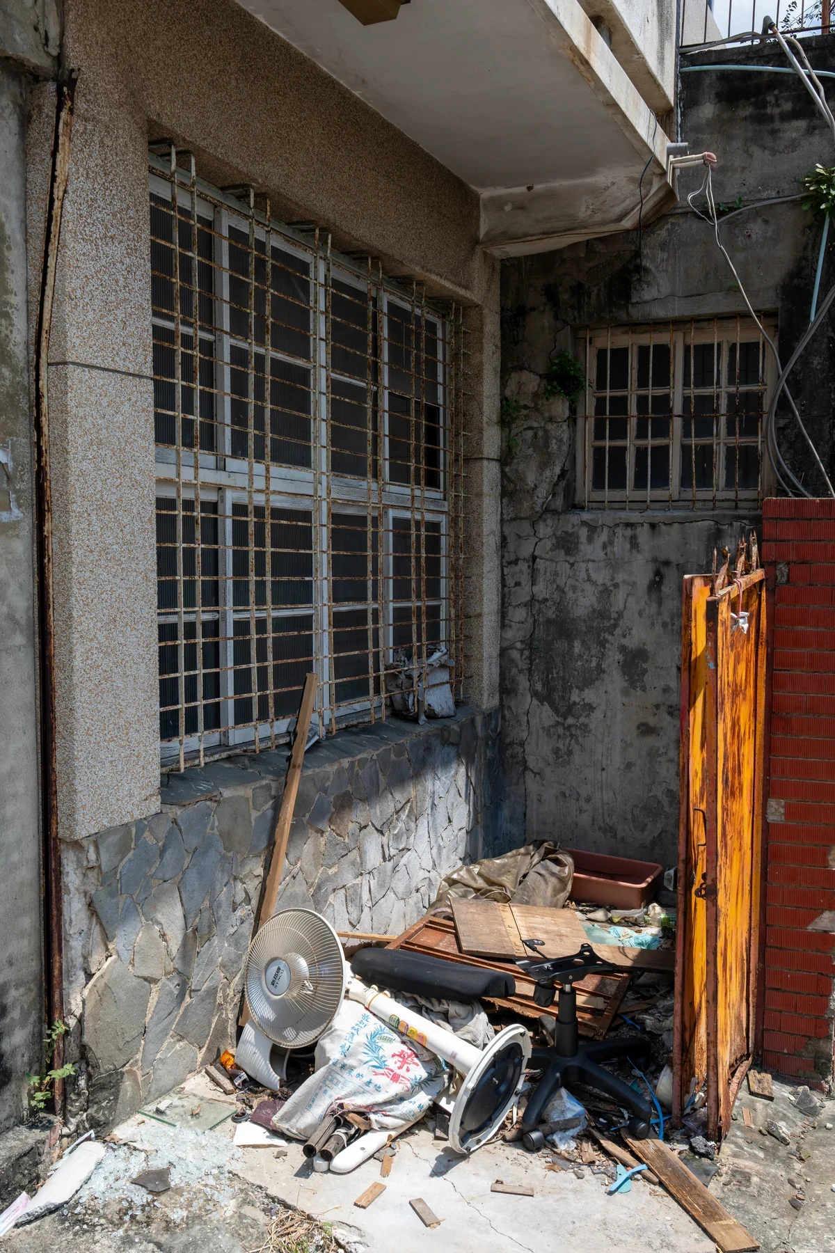Discarded objects, a fan and boxes beneath barred windows beside an orange gate