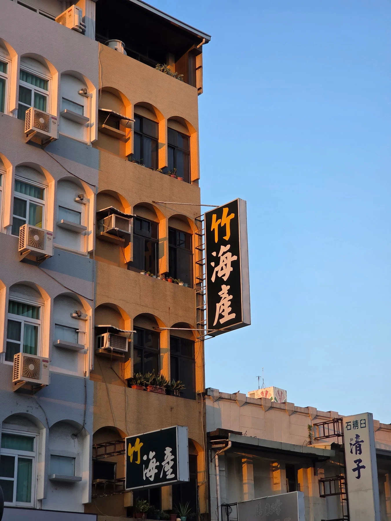 Warm evening light on arched windows and a projecting sign in Tainan