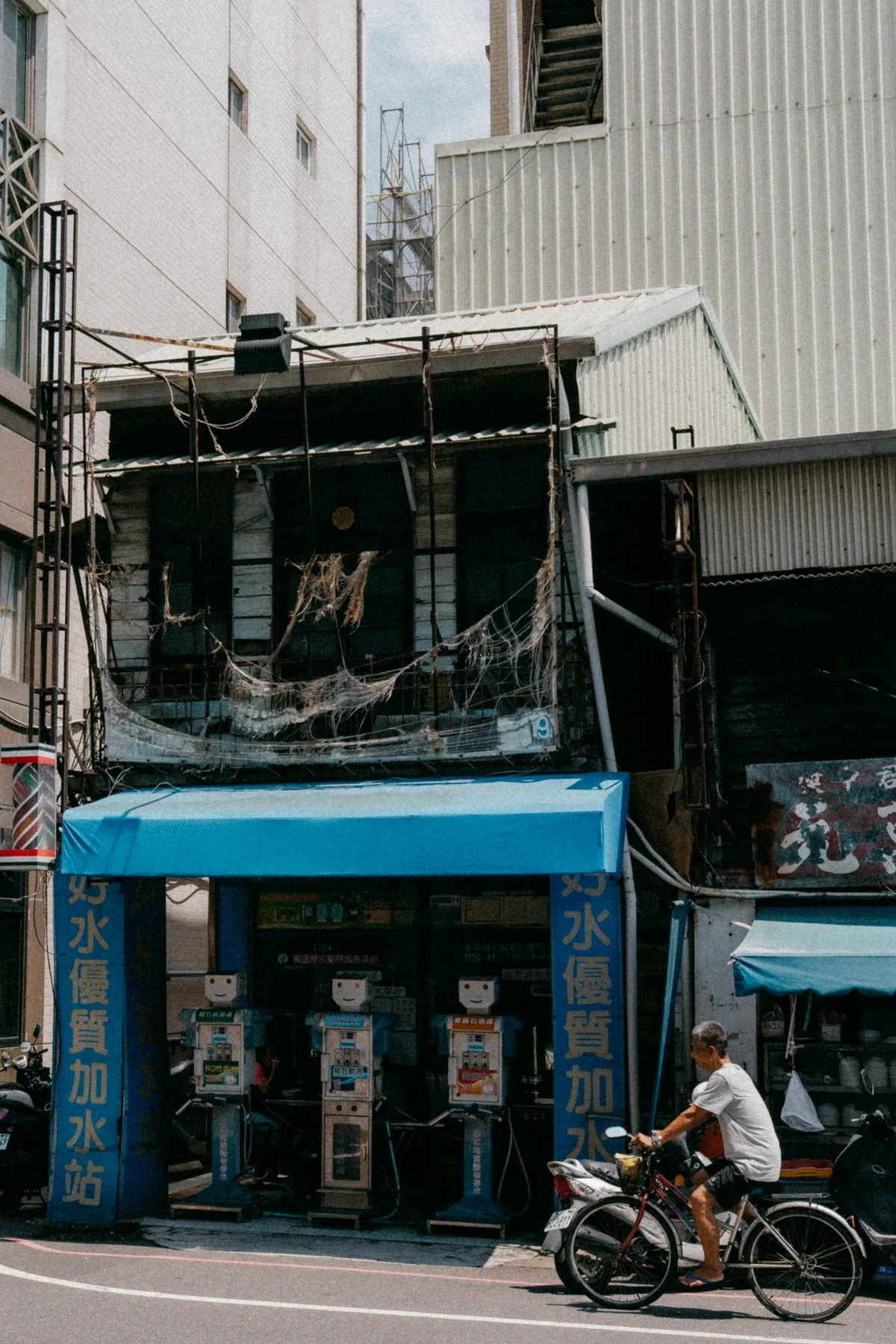 A cyclist passing a narrow blue-fronted shop beneath weathered upper floors