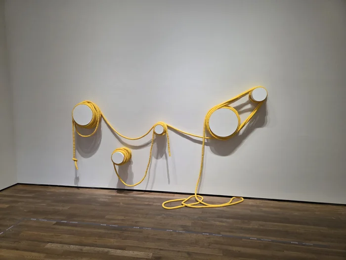 A yellow cord installation looping between white fixtures on a gallery wall